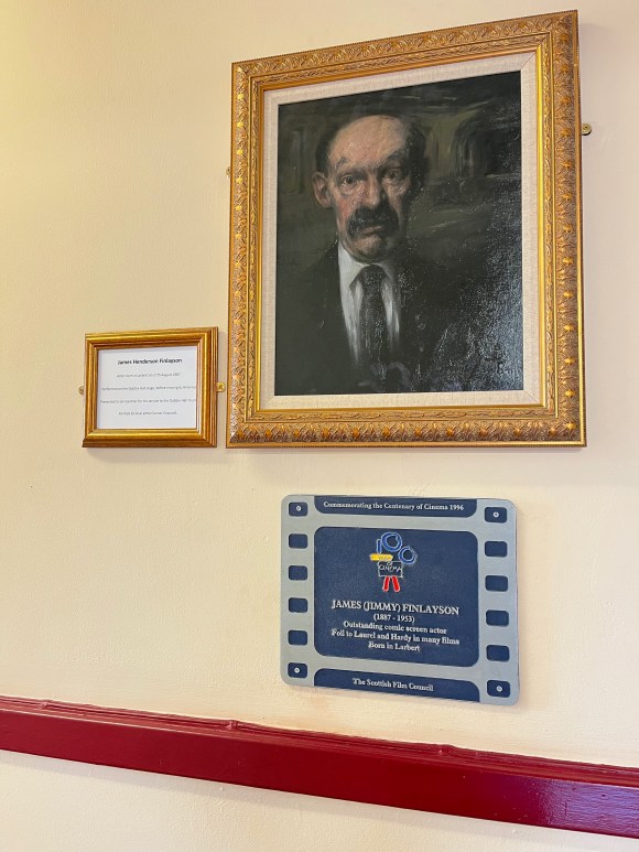The portrait of James Finlayson hanging in the Dobbie Hall alongside his 1996 Scottish Film Council plaque